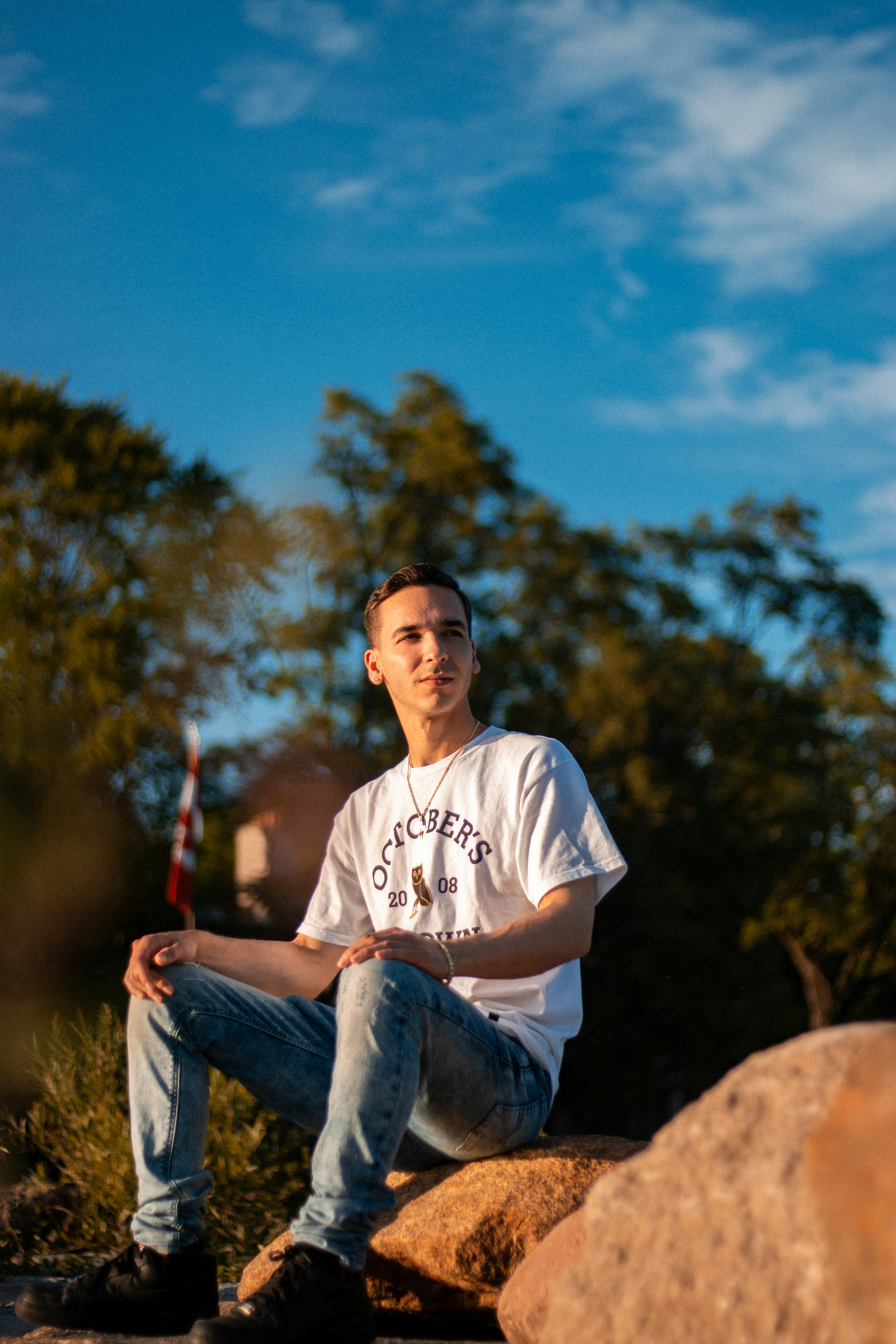 man in white crew neck t-shirt and blue denim jeans sitting on brown rock during